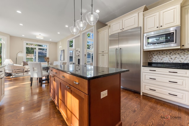 kitchen with dark wood-type flooring, built in appliances, decorative backsplash, a kitchen island, and dark stone countertops