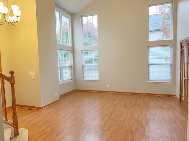 unfurnished room featuring a chandelier, a towering ceiling, and light hardwood / wood-style flooring