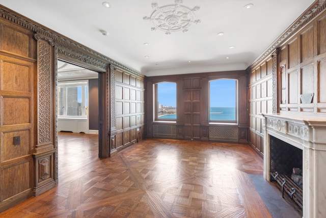 unfurnished living room featuring wood walls, a water view, and dark parquet flooring