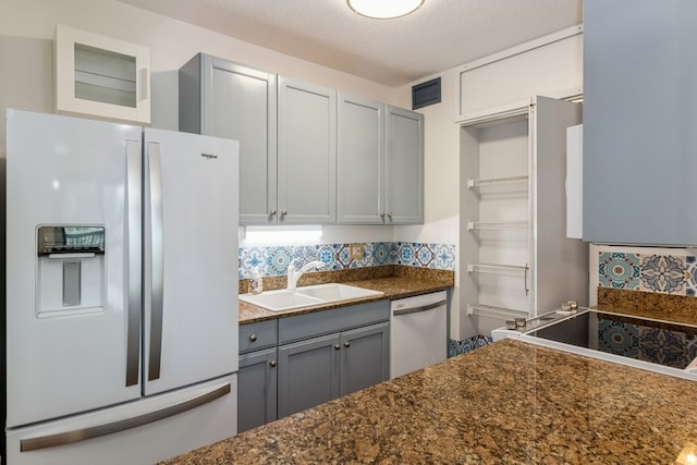 kitchen with a textured ceiling, gray cabinets, white fridge with ice dispenser, sink, and dishwasher