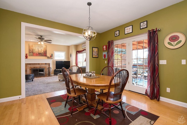 dining room with a tiled fireplace, light hardwood / wood-style floors, and ceiling fan with notable chandelier