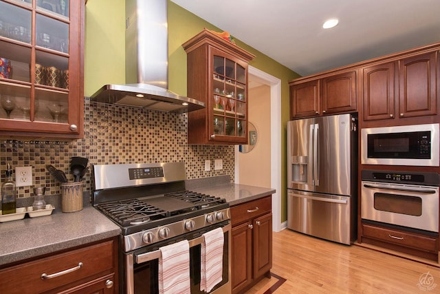 kitchen featuring backsplash, light hardwood / wood-style flooring, stainless steel appliances, and wall chimney range hood