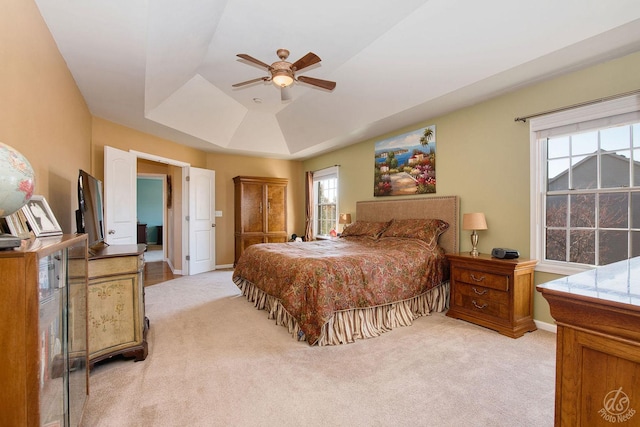 bedroom featuring a raised ceiling, ceiling fan, and light carpet