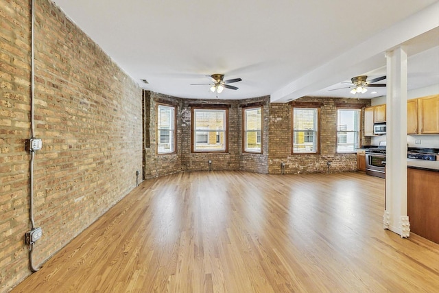 unfurnished living room with brick wall, ceiling fan, light hardwood / wood-style floors, and plenty of natural light