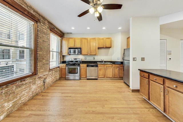 kitchen with appliances with stainless steel finishes, light hardwood / wood-style flooring, sink, ceiling fan, and brick wall