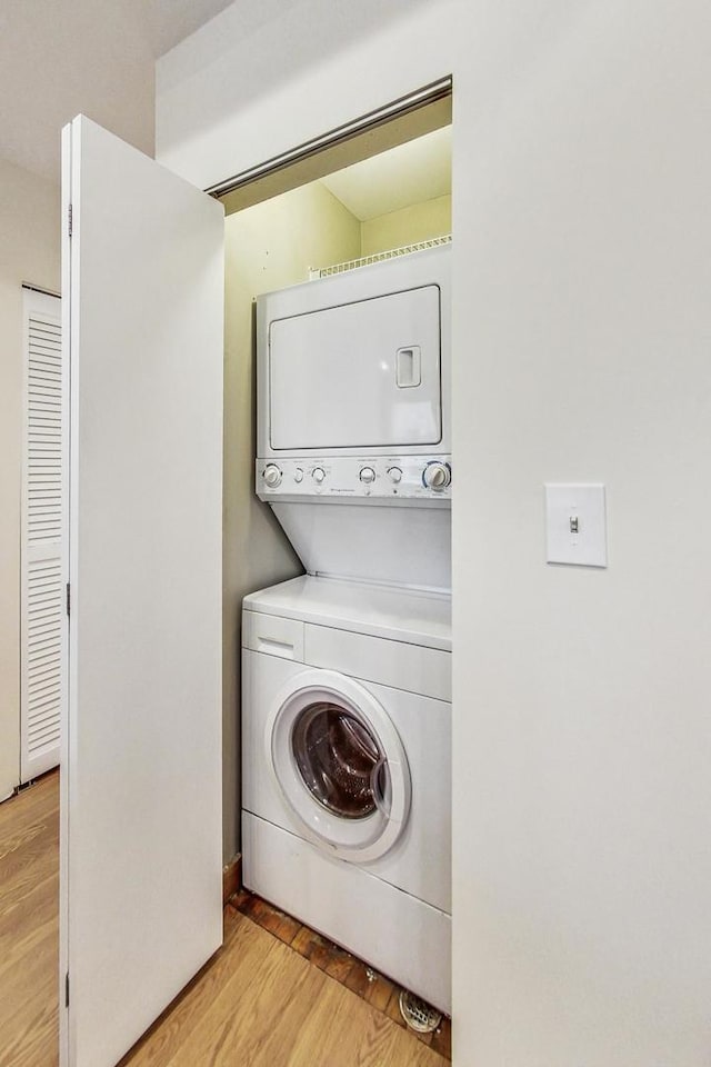 clothes washing area with light wood-type flooring and stacked washer and dryer