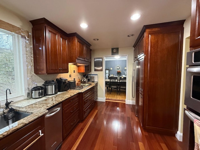 kitchen featuring decorative backsplash, appliances with stainless steel finishes, dark hardwood / wood-style flooring, light stone countertops, and sink