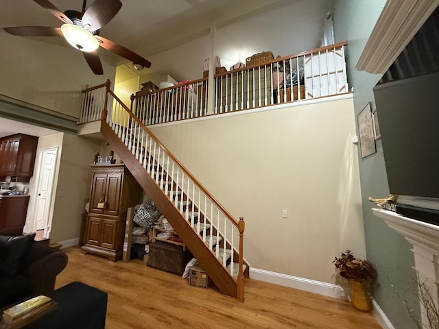 staircase with hardwood / wood-style floors, a towering ceiling, and ceiling fan