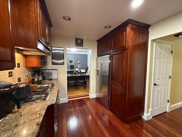 kitchen with light stone countertops, backsplash, stainless steel appliances, and dark wood-type flooring