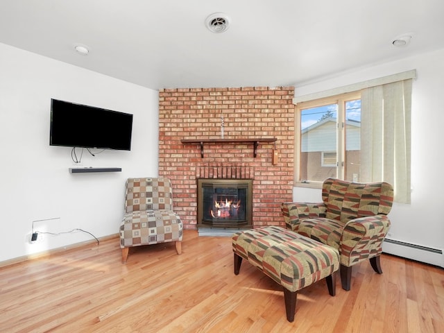 living area with a brick fireplace, light hardwood / wood-style floors, and a baseboard radiator