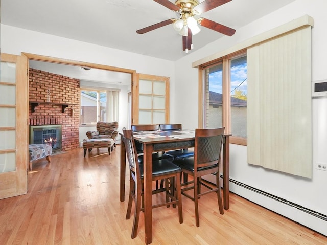 dining area featuring a brick fireplace, a baseboard radiator, light hardwood / wood-style floors, and ceiling fan