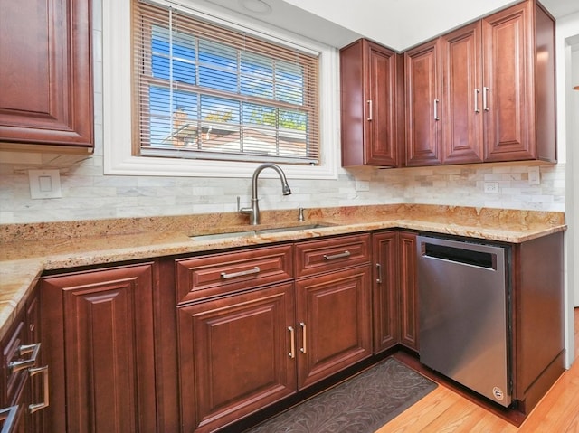 kitchen featuring stainless steel dishwasher, sink, light stone countertops, and light hardwood / wood-style flooring