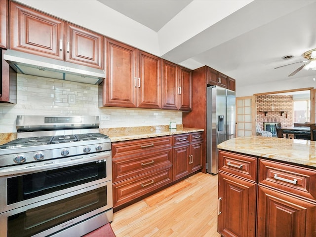 kitchen featuring tasteful backsplash, range hood, appliances with stainless steel finishes, light stone countertops, and light hardwood / wood-style flooring