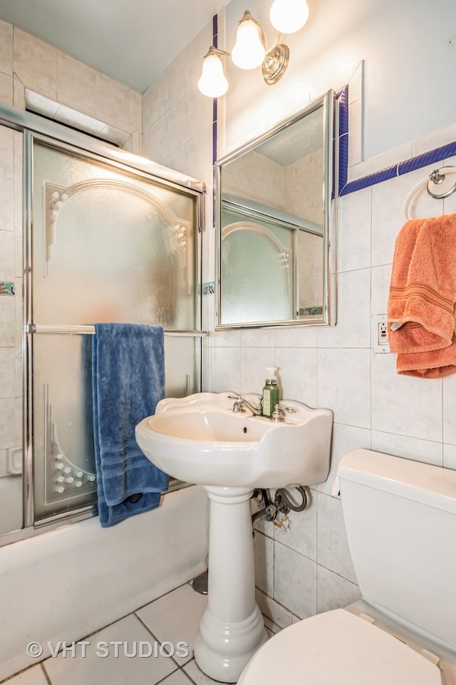 bathroom featuring toilet, tile walls, tile patterned flooring, and shower / bath combination with glass door