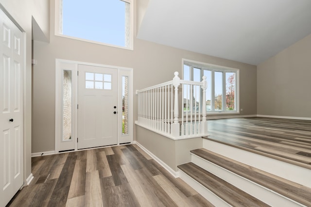 foyer entrance with stairway, a towering ceiling, baseboards, and wood finished floors