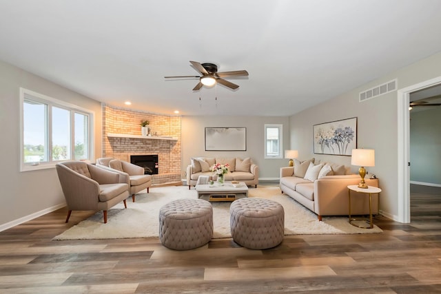 living room with visible vents, a brick fireplace, baseboards, wood finished floors, and a ceiling fan