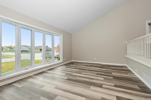 empty room with vaulted ceiling, wood finished floors, visible vents, and baseboards