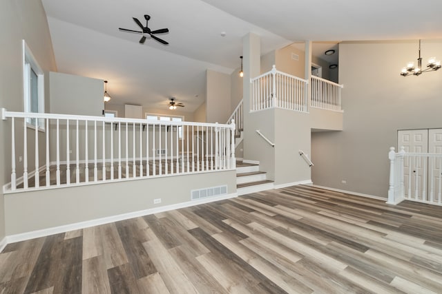 unfurnished living room featuring wood-type flooring, ceiling fan with notable chandelier, and high vaulted ceiling