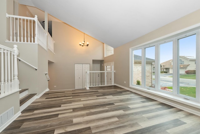 unfurnished living room featuring visible vents, high vaulted ceiling, wood finished floors, stairway, and an inviting chandelier