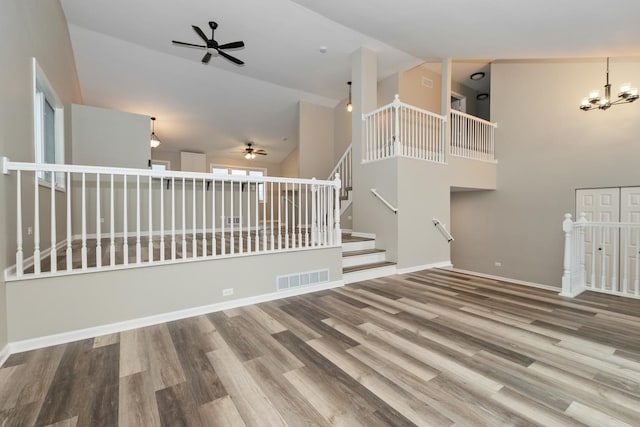 unfurnished living room with visible vents, baseboards, ceiling fan with notable chandelier, wood finished floors, and high vaulted ceiling