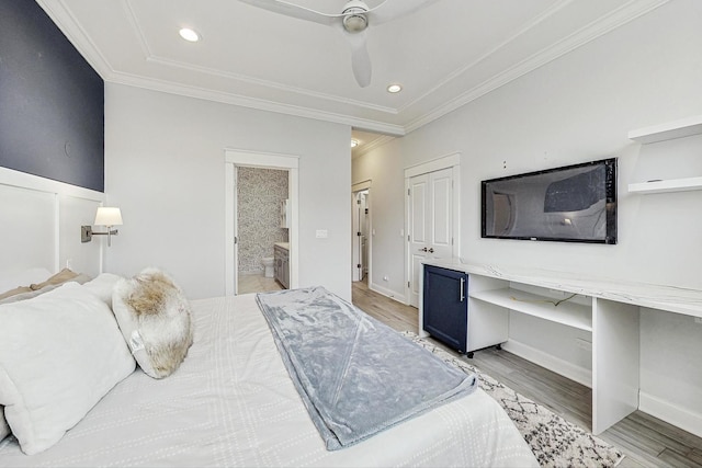 bedroom with ceiling fan, connected bathroom, built in desk, ornamental molding, and light hardwood / wood-style floors