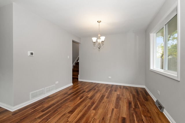 spare room with dark hardwood / wood-style flooring and an inviting chandelier