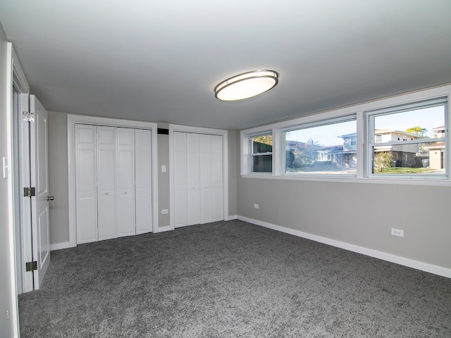 unfurnished bedroom featuring dark colored carpet and two closets