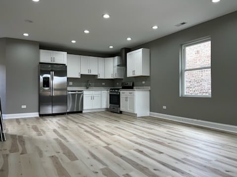 kitchen featuring white cabinets, sink, wall chimney range hood, light wood-type flooring, and appliances with stainless steel finishes