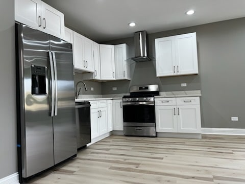 kitchen featuring sink, appliances with stainless steel finishes, wall chimney exhaust hood, white cabinets, and light wood-type flooring