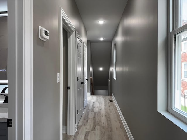 hallway featuring visible vents, light wood-style flooring, and baseboards