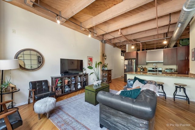 living room with beamed ceiling, light hardwood / wood-style flooring, rail lighting, and sink