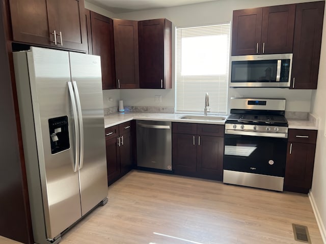 kitchen featuring dark brown cabinets, sink, light hardwood / wood-style flooring, and appliances with stainless steel finishes