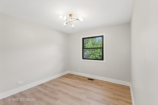 spare room featuring light wood-type flooring and a notable chandelier