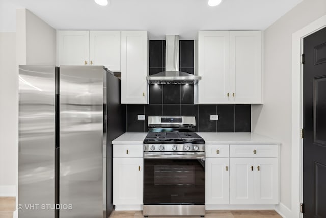 kitchen featuring white cabinets, decorative backsplash, appliances with stainless steel finishes, and wall chimney range hood