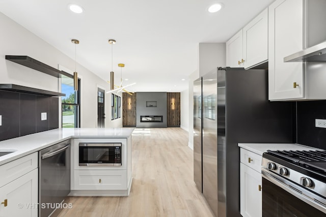 kitchen featuring stainless steel appliances, light hardwood / wood-style floors, wall chimney exhaust hood, white cabinetry, and decorative light fixtures