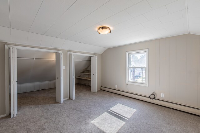 unfurnished bedroom featuring baseboard heating, vaulted ceiling, and light colored carpet