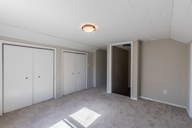 unfurnished bedroom featuring light colored carpet, vaulted ceiling, and two closets