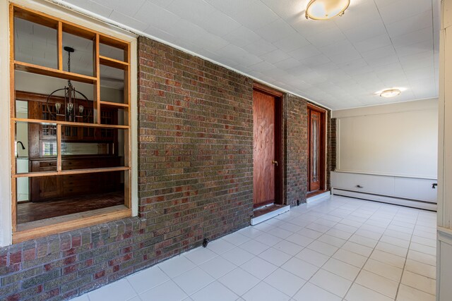 tiled empty room featuring baseboard heating and brick wall