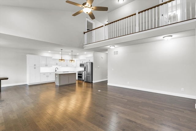 unfurnished living room with a towering ceiling, dark hardwood / wood-style flooring, and ceiling fan