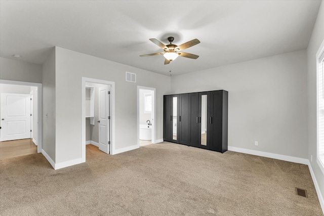 unfurnished bedroom featuring multiple windows, light colored carpet, ceiling fan, and ensuite bathroom