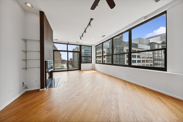 unfurnished room featuring ceiling fan, light wood-type flooring, and a wall of windows