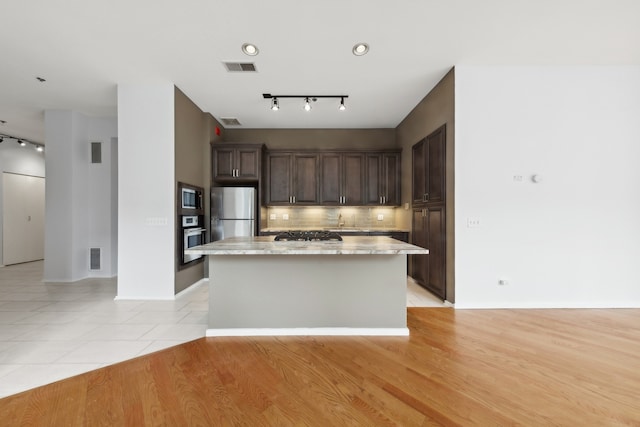 kitchen with stainless steel appliances, sink, light stone counters, a kitchen island, and light wood-type flooring