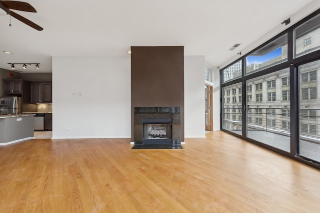 unfurnished living room featuring ceiling fan, a wall of windows, track lighting, and light wood-type flooring