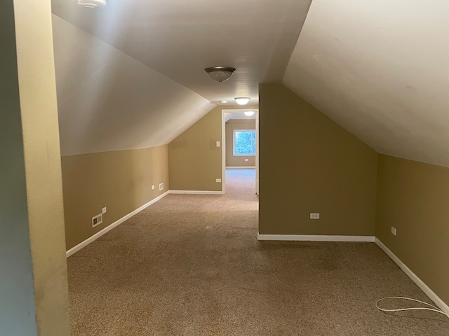 additional living space featuring light colored carpet and vaulted ceiling