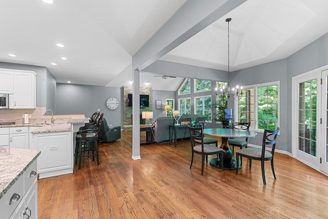 dining space with hardwood / wood-style floors, ceiling fan with notable chandelier, sink, and vaulted ceiling