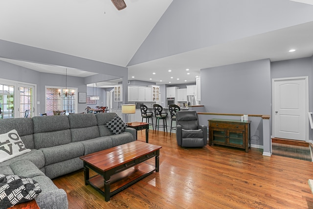 living room featuring wood-type flooring, ceiling fan with notable chandelier, and high vaulted ceiling