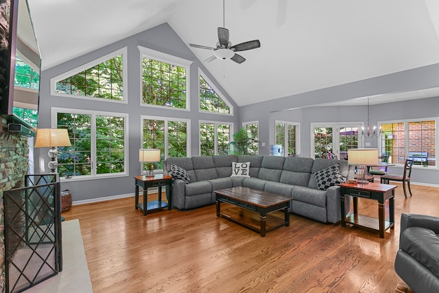 living room with a wealth of natural light, ceiling fan with notable chandelier, high vaulted ceiling, and hardwood / wood-style flooring