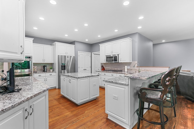 kitchen featuring light stone counters, light wood-type flooring, appliances with stainless steel finishes, white cabinets, and a center island