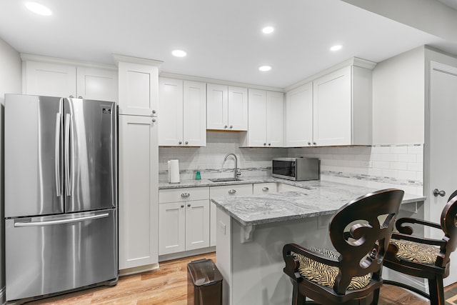 kitchen featuring light hardwood / wood-style floors, white cabinetry, sink, appliances with stainless steel finishes, and a kitchen breakfast bar