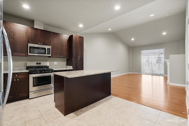 kitchen with light stone counters, a center island, vaulted ceiling, light hardwood / wood-style flooring, and appliances with stainless steel finishes